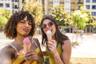 Two cheerful women enjoying ice cream cones outdoors, taking a selfie on a sunny summer day in an