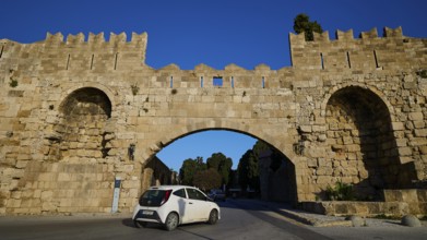 Arsenal Tor, Modern car drives through a historic stone gate on the road, harbour area, Rhodes