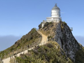 Nugget Point Lighthouse with Nugget Rocks in front of a blue sky, South Island, New Zealand,