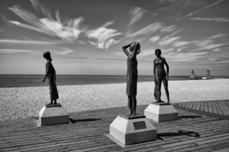 Bronze sculpture La Heure du Bain by Dominique Denry on the beach, sky, blue, behind it beacon Feu
