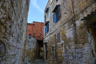 Winding old alleyway with stone façade and blue shutters in historic surroundings, Rhodes Old Town,