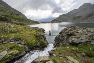 Mountaineer standing on a suspension bridge, mountain stream and mountain lake Wangenitzsee,