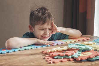 Boy with autism, expresses frustration, playing with puzzle pieces, on a wooden table, natural