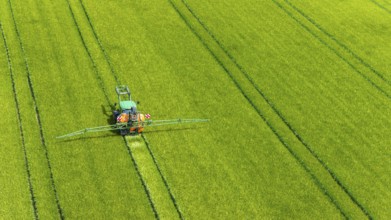 Farmer with tractor working in the field. In early summer, he fertilises the grain for an optimum