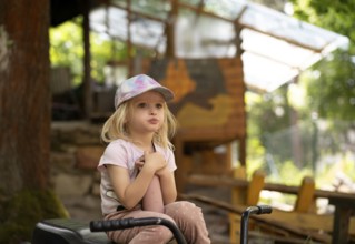 Girl, 3 years, blonde, sitting on bicycle in the garden, pensive, summer, Stuttgart,