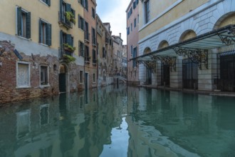 Calm water reflecting colorful buildings along a canal in venice, italy, during acqua alta, or high