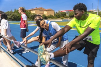 Track and field athletes stretching their legs on a railing by the track, preparing for a