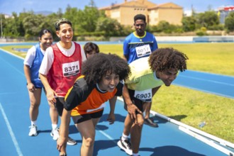 Diverse group of athletes crouching at starting line, preparing for a race on a blue running track