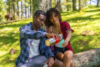 Young couple sharing a hot drink from a thermos while taking a break during their hike in a sunny