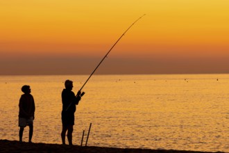 A man fishing just in front of sunrise on the Costa Rei, a coastline of the Italian island of