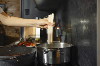 A person prepares a healthy pasta dish by adding uncooked noodles to boiling water in a