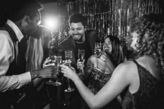 Happy friends are toasting with champagne flutes, enjoying nightlife together at a glamorous party