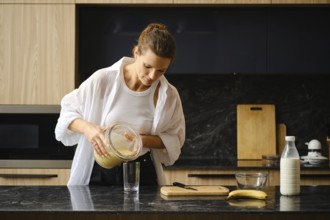 A person is preparing a healthy smoothie by pouring a blended mixture of banana and sea buckthorn