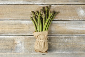 A bundle of fresh green asparagus is wrapped in brown paper and tied with twine, resting on a