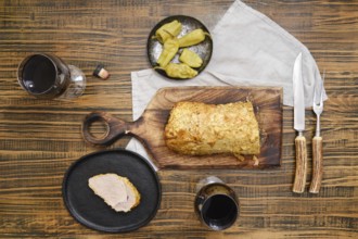 Overhead view of roasted pork meat and pickled peppers on a wooden table accompanied with red wine