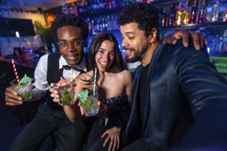 Happy friends taking a selfie while drinking cocktails at the bar, having fun together on a night