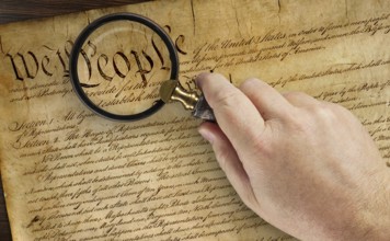 Male hand holding magnifying glass over the work people on the United States constitution
