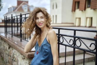 A stylish woman enjoys a relaxed moment outdoors, leaning against a stone railing while smiling at