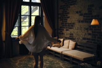 A woman in a light outfit twirls gracefully in a dimly lit room. Sunlight filters through large