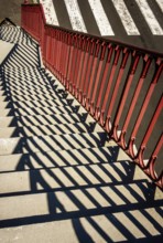 Bright sunlight creates intriguing patterns as shadows fall from red railings onto stone steps next
