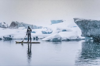 Man stand up paddling, snowfall, glacier lagoon Jökulsarlon at Vatnajökull, Iceland* Man stand up