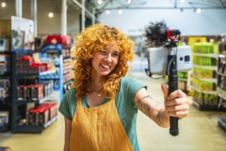 Young woman working as supermarket clerk vlogging using smartphone and microphone promoting