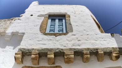 A single blue window on a rustic white building under a clear sky, Mantomata stones, Chora, UNESCO