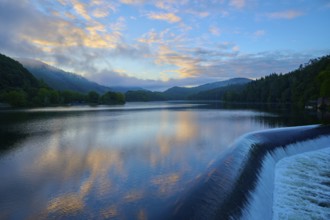 Calm lake with dam Paulushof-Absperrdamm, at dusk, surrounded by mountains and forests under a