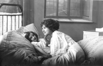 Woman with daughter, 1920s, A mother lies down with her child in bed, showing affection in a cosily