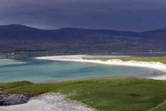 A tranquil beach with turquoise waters and dark, cloudy skies at the foot of mountains, Isle of