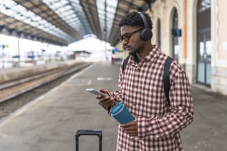 Stylish commuter using a mobile phone while enjoying music through headphones at a bustling train