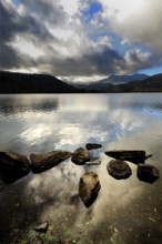 Serene waters reflect the cloudy sky at Lake Chambon, surrounded by mountains in