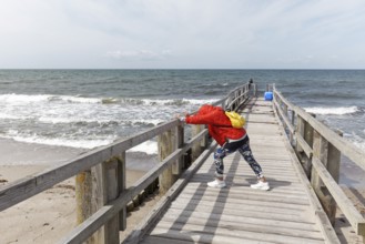Woman in padded jacket doing stretching exercise with lunge on a wooden walkway on the beach,