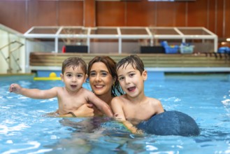 Mother and two sons smiling and playing in a swimming pool, enjoying a family moment of fun and