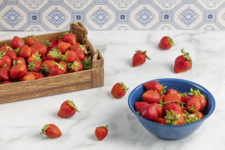 Fresh strawberries in a blue bowl and a cardboard box on a marble slab