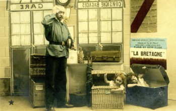 2 children in boxes, 1920, A man poses in a railway station environment while children humorously