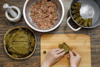 Grape leaves are being filled with a savory mixture of minced meat and rice at a home kitchen