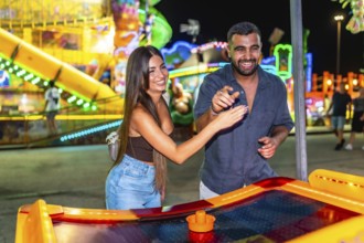 Young couple enjoying a game of air hockey at a brightly lit amusement park, adding excitement to