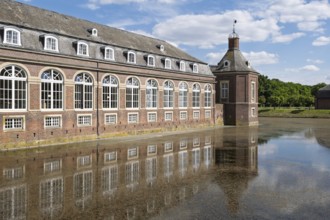 Historic brick building reflected in calm water under a blue sky and clouds, Nordkirchen Castle,