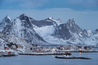 Fishermen's Village in front of snowy mountain range at the coastline in winter, Lofoten, Norway