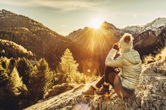 Woman sitting thoughtfully at a feslen at autumn atmosphere during sunset in the Swiss Alps in the