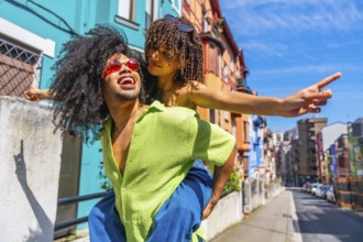 Happy tourists having fun piggybacking in a colorful city street, enjoying summer holidays and