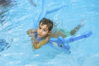 Young boy swimming in a pool, happily playing with an inflatable toy dolphin, enjoying the