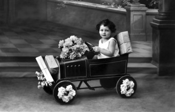 Child in toy car, 1920s, A child drives a toy car, decorated with flowers, in a nostalgic black and