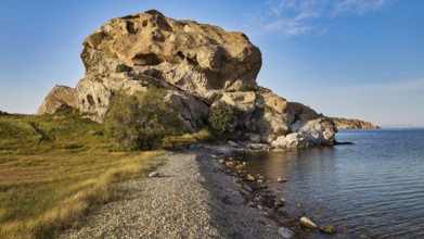 Large rock formation on the coast with clear sky and grassy areas in the foreground, Rock of