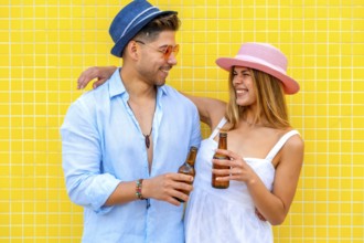 Young tourists drinking bottled beer, wearing summer clothes and hats, smiling and having fun on a
