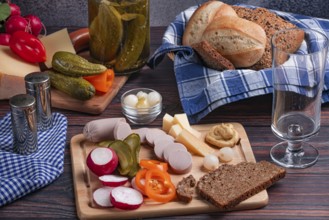 Rustic snack with sausage, cheese, vegetables, mustard and bread on a laid table