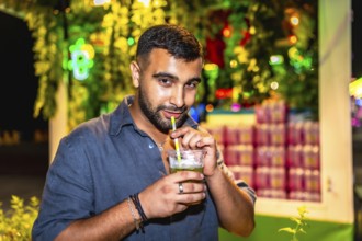 Young man sips a mojito through a straw at a vibrant night market, enjoying the festive atmosphere