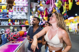 Happy friends playing at a throwing game stall trying to win plush toys at amusement park at night