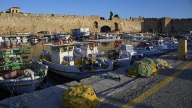 Boats moored in the harbour in front of an old wall under a blue sky, Rhodes Old Town, Rhodes,